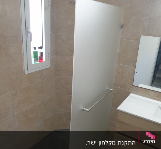 מקלחון עם דלת זכוכית ומדף עם בקבוקי שמפו